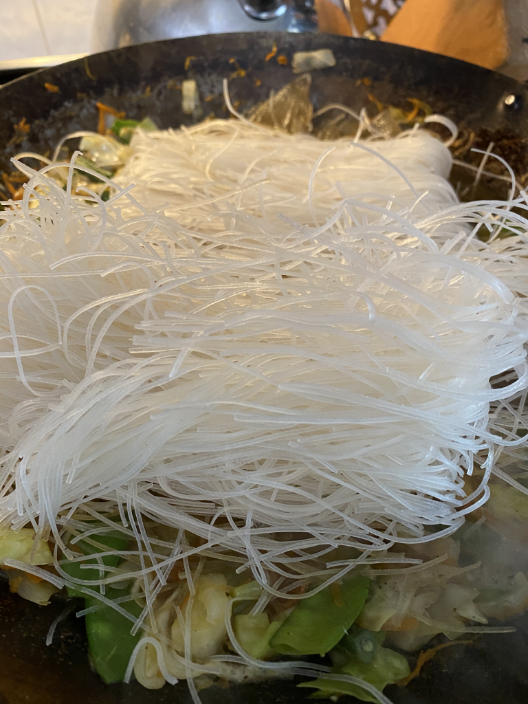 Rice noodles being added to wok. The extra liquid will soften the noodles and thicken the gluten-free Pancit. 
