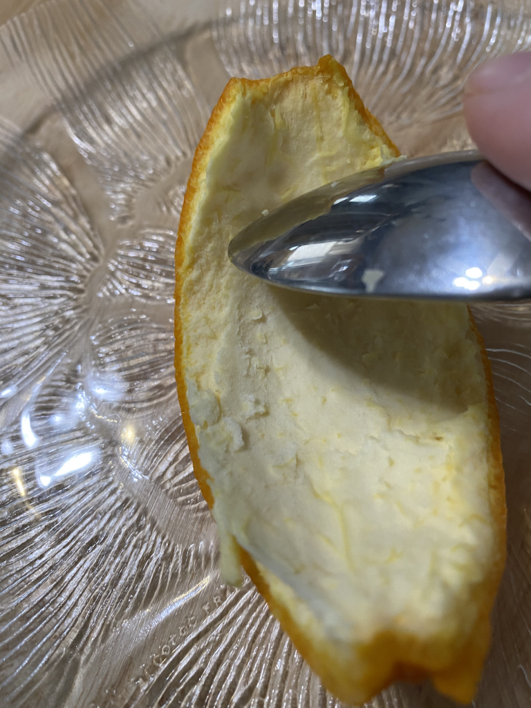 Using the edge of the spoon to remove some of the white pith of the orange peels. 