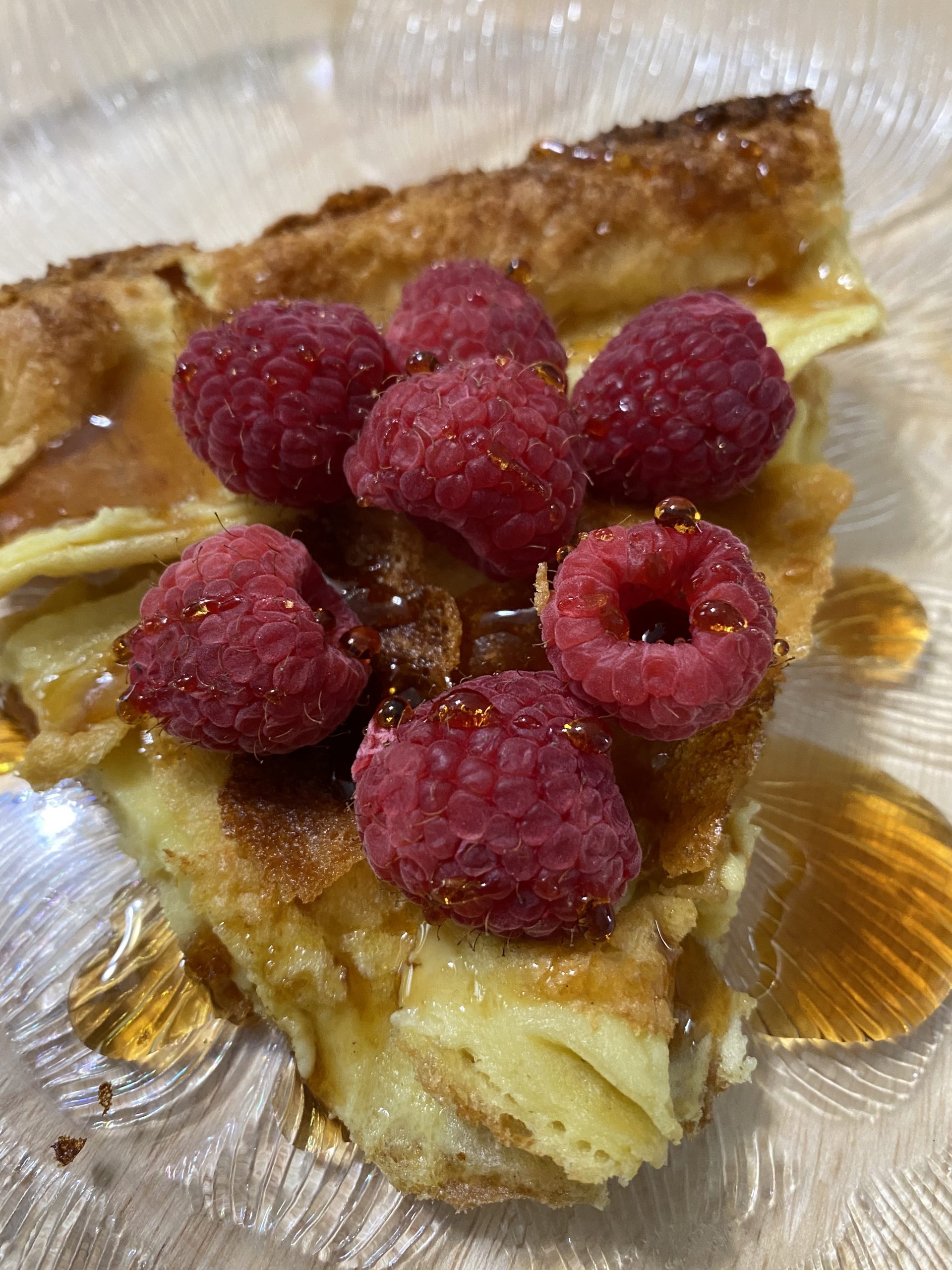 Slice of Dutch baby with maple syrup and raspberries
